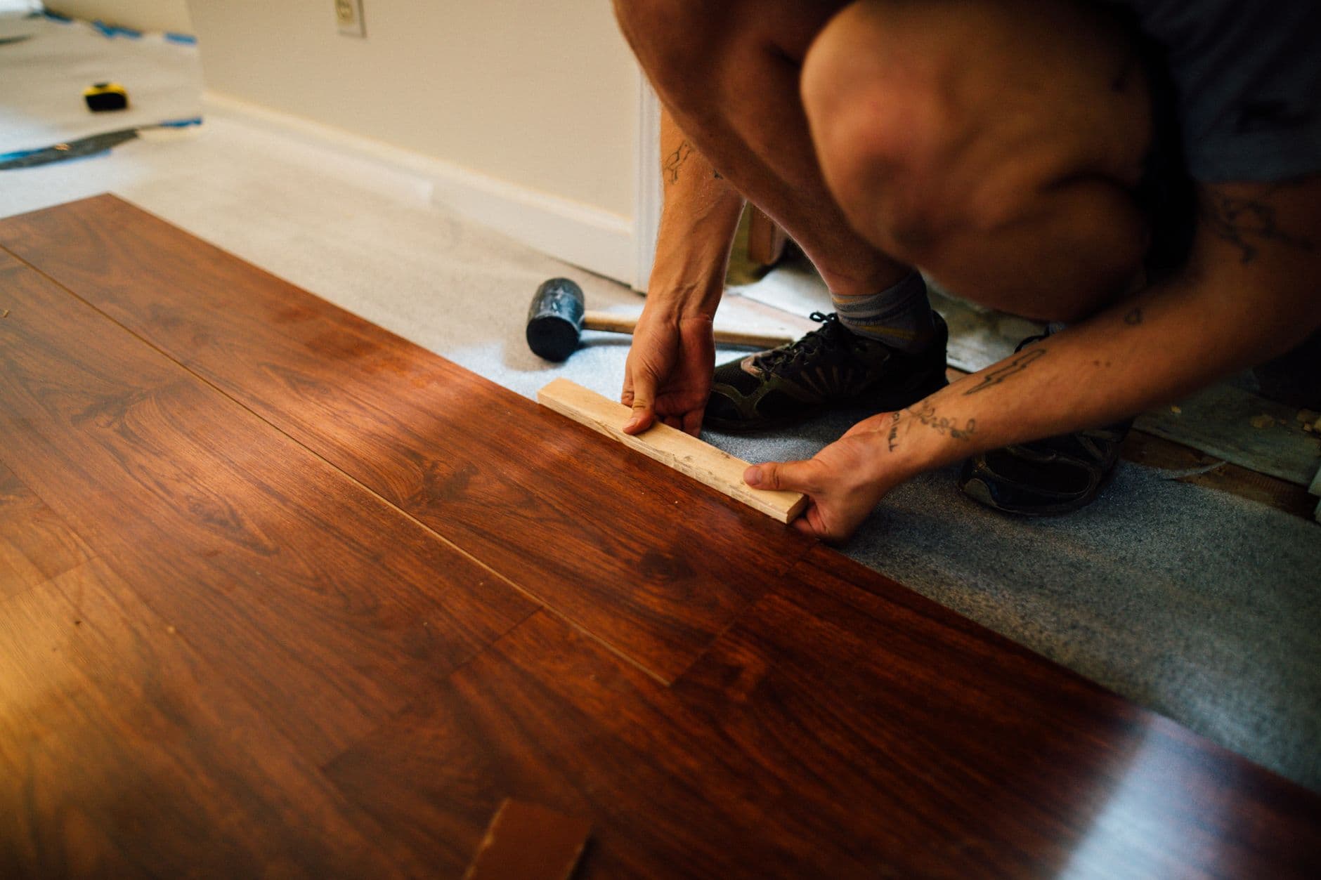 Tradesperson laying engineered timber floorboards with a tapping block over underlay