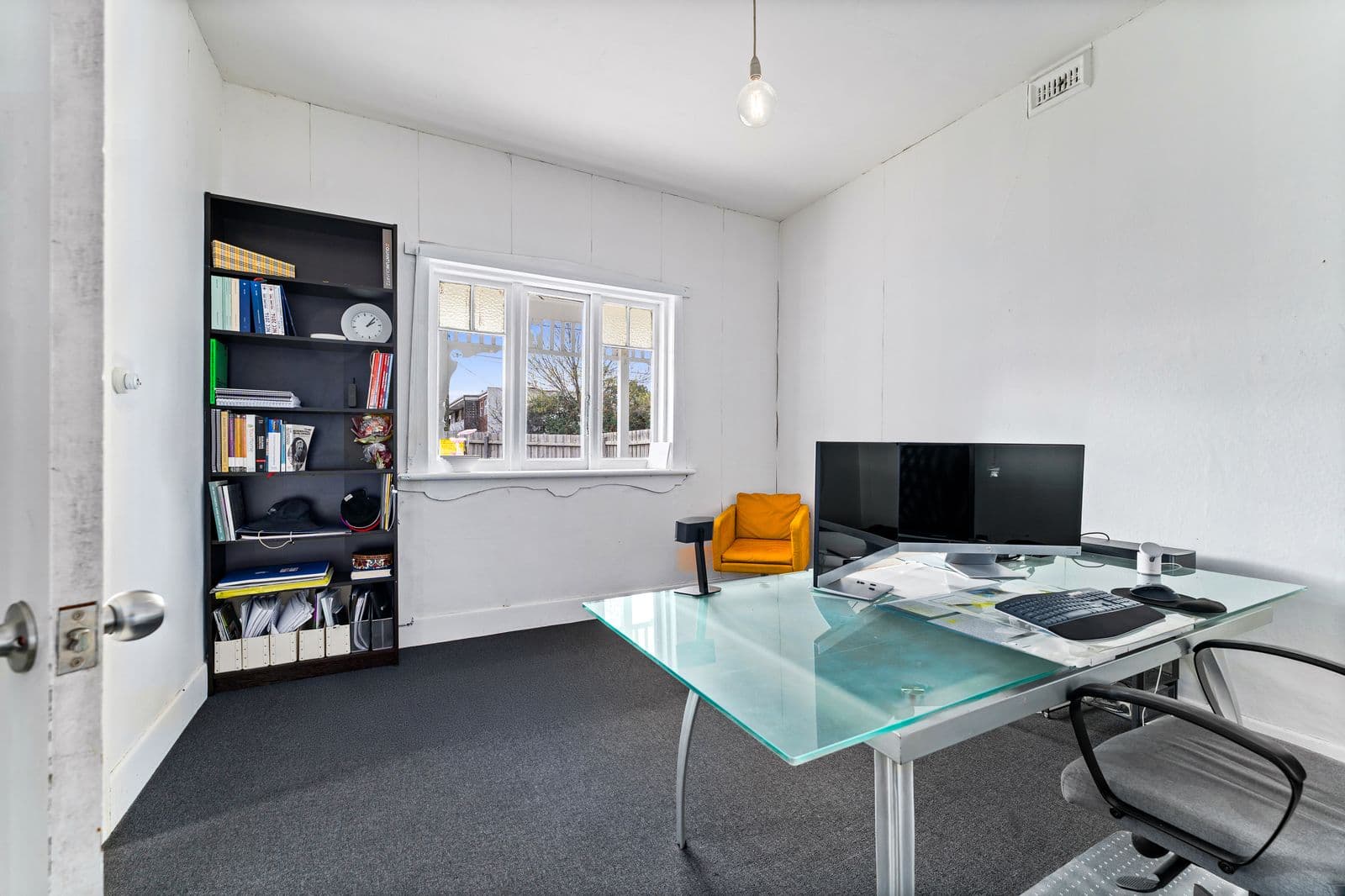 Ballarat Road office interior - glass desk, dual monitors, bookshelf and dark carpet