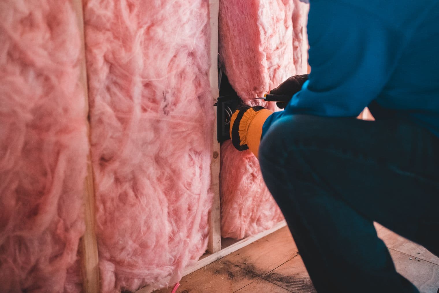 Tradesperson fitting insulation batts and an electrical outlet box into a stud wall